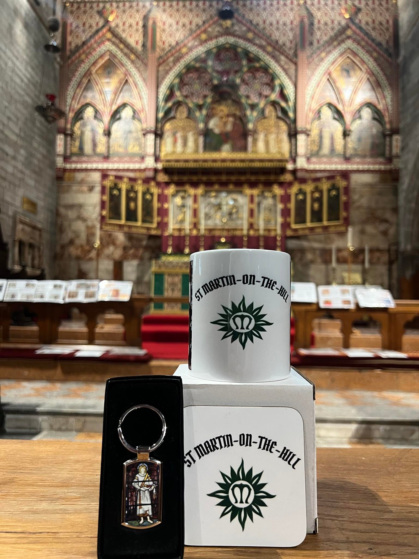 White mug with 'St Martin on the Hill' logo and keychain in front of a church interior.