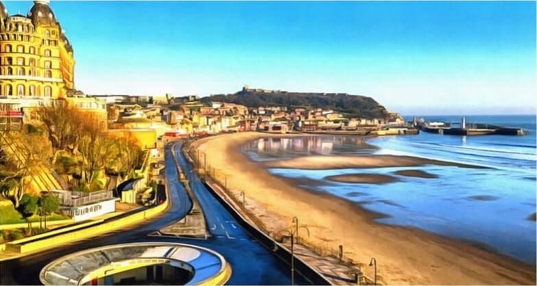 Scenic view of Scarborough's South Bay coastline with sandy beach and historic buildings.